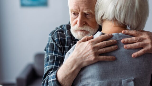 Back View Of Senior Woman Hugged By Husband, Sick On Dementia